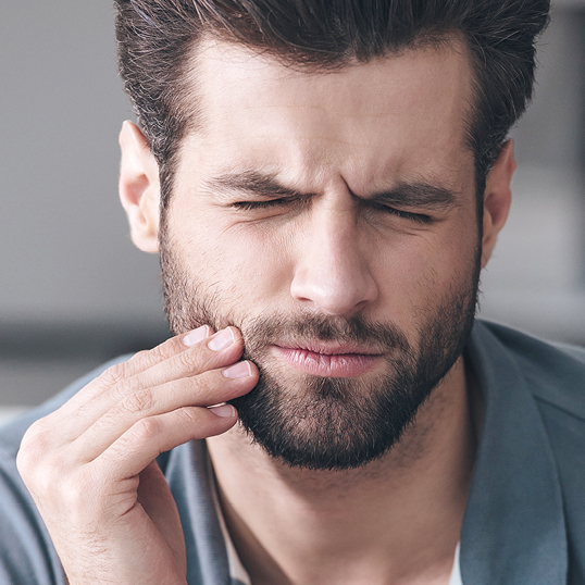 Zahnschmerzen - Mann greift sich mit schmerzverzerrtem Gesicht an die Wange